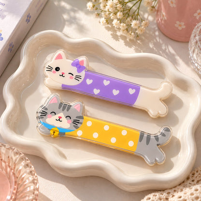 Kittens Love hair clips flat lay: white cat with a purple bow in a heart jumper and grey tabby with a bell in a yellow polka-dot jumper